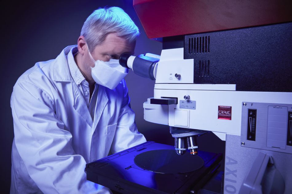 A scientist at a CRAIC microspectrophotometer, a wafer on the stage under ultraviolet illumination